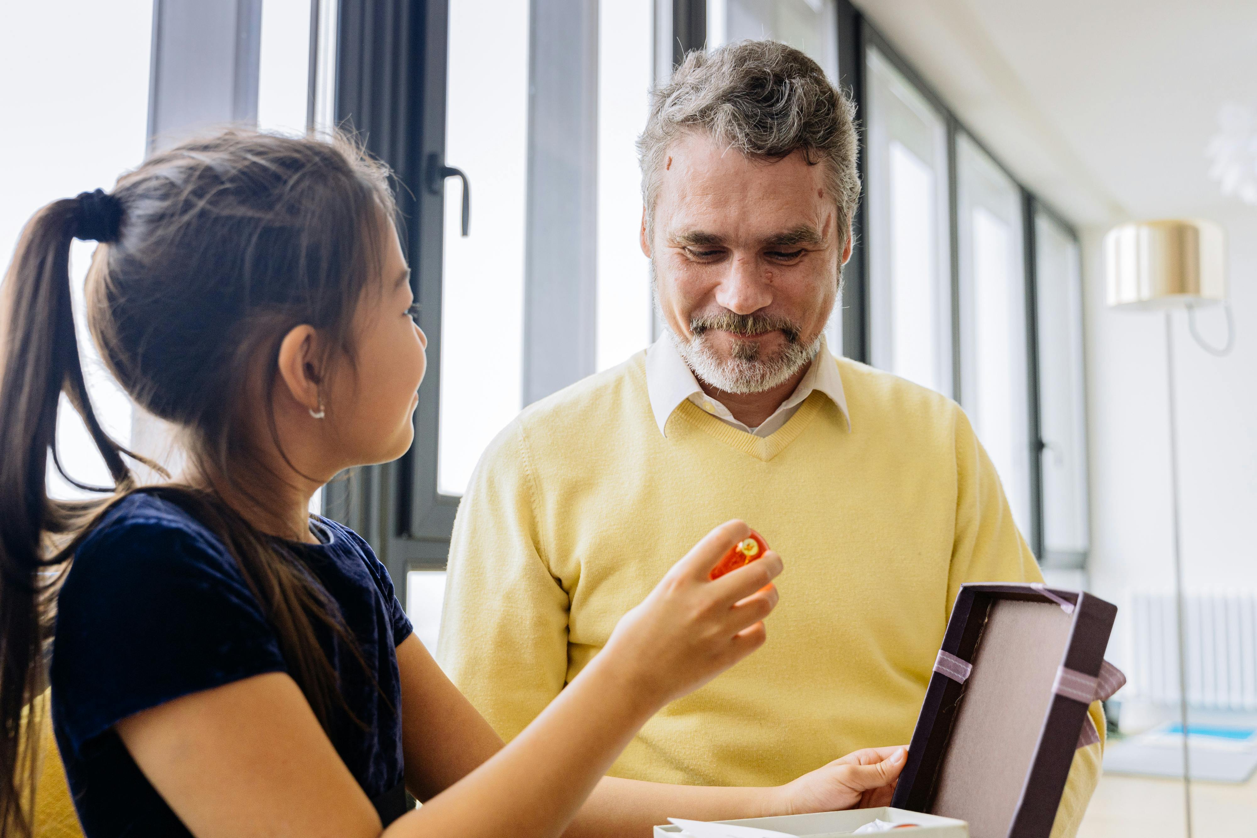 Hombre de 45-50 años sonriendo al abrir un regalo minimalista en un salón moderno con luz cálida